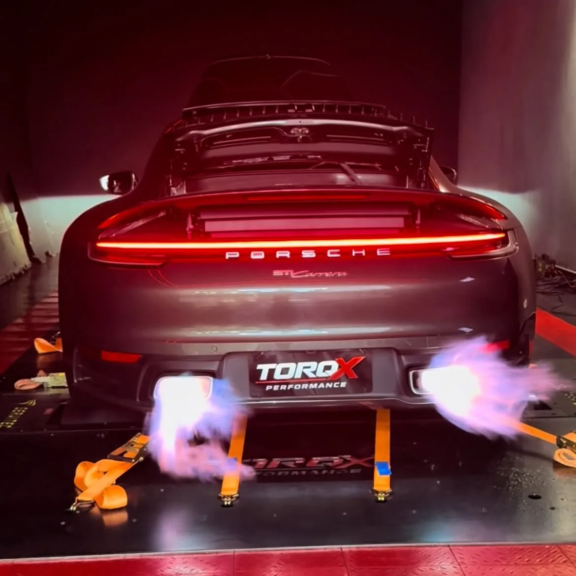 Traseira de um Porsche 911 em ensaio de dinamômetro, com chamas duplas saindo do escapamento e placa TORQX Performance