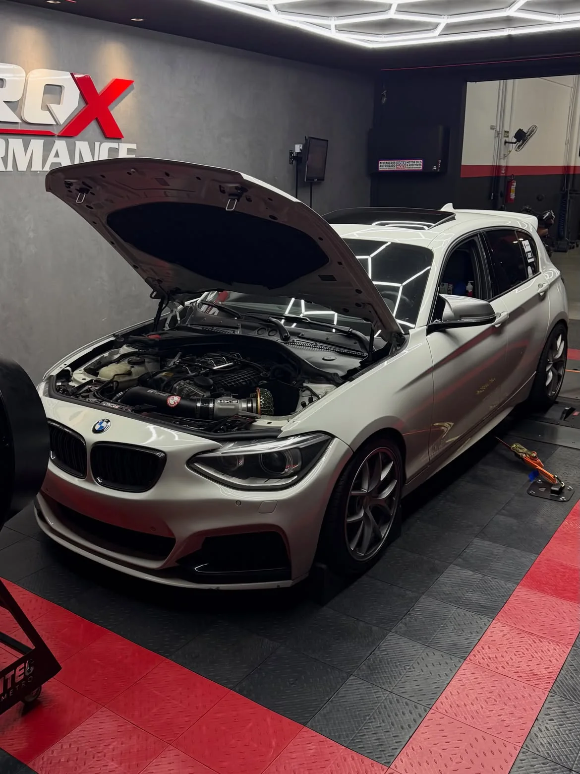BMW Série 1 branco em três quartos dianteiro com o capô levantado, letreiro TORQX ao fundo