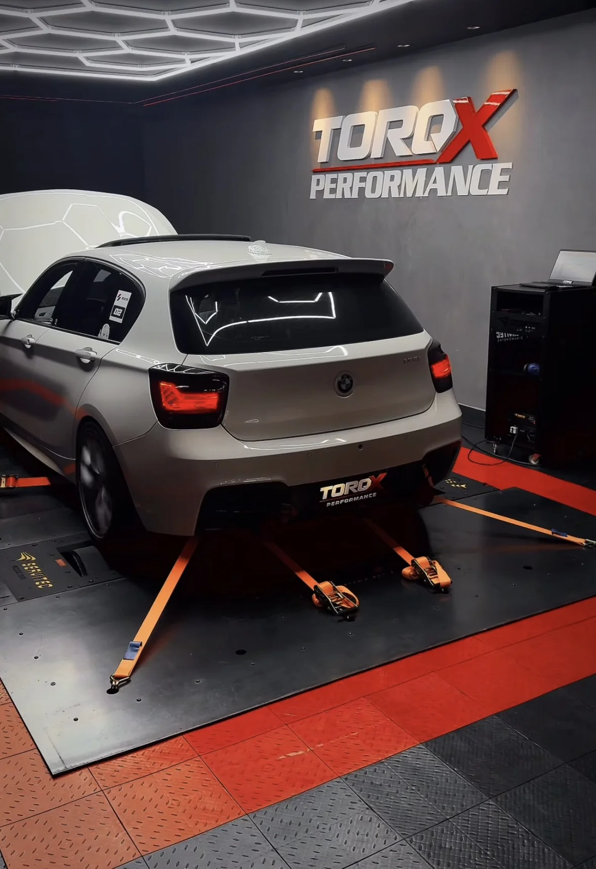 Traseira do BMW Série 1 champagne vista de ângulo alto, com as cintas laranja de ancoragem