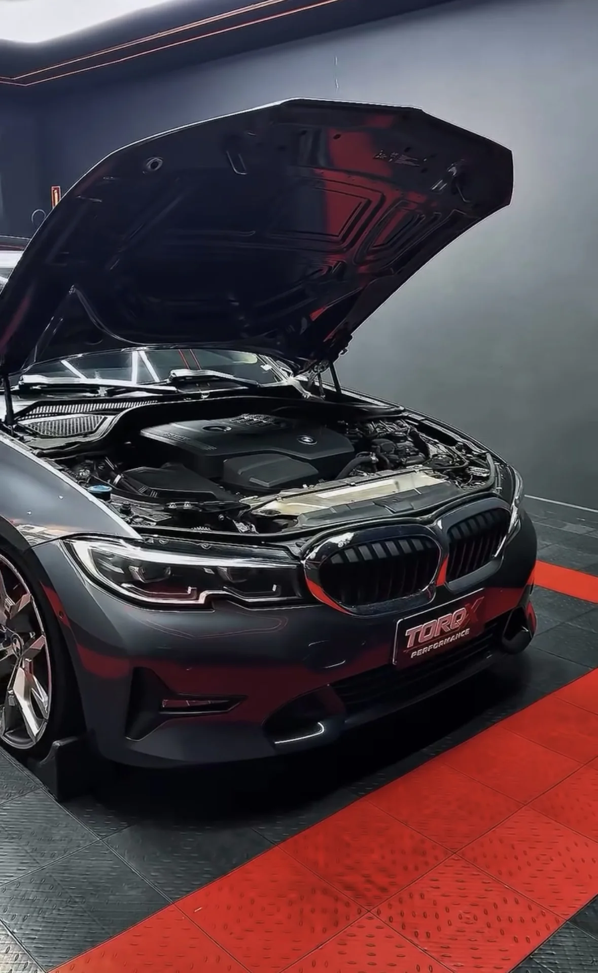 BMW Série 3 cinza com o capô levantado na sala de dinamômetro, vão do motor exposto