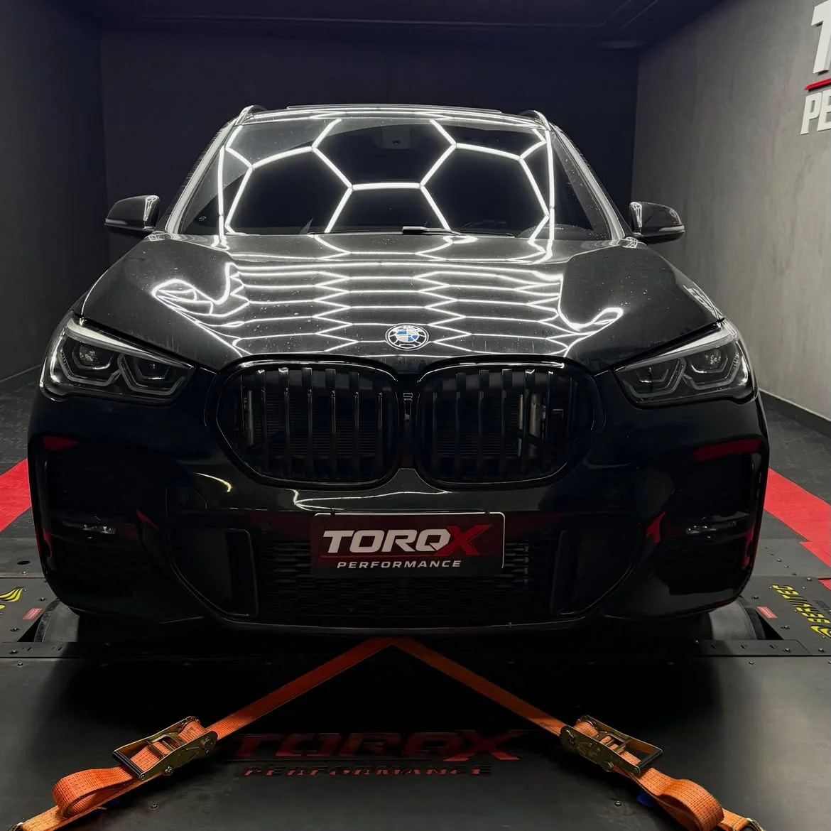 BMW X1 preto de frente, simétrico, com a malha hexagonal da luminária refletida no capô
