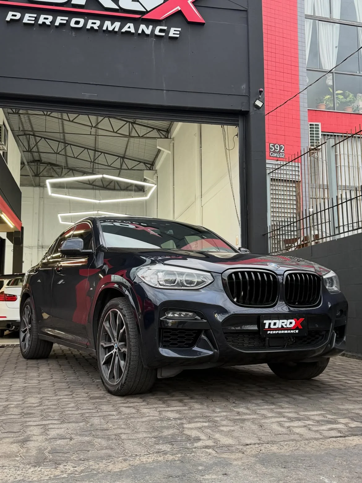 BMW X4 preto de três quartos dianteiro em frente ao portão da TORQX, com o letreiro da fachada acima