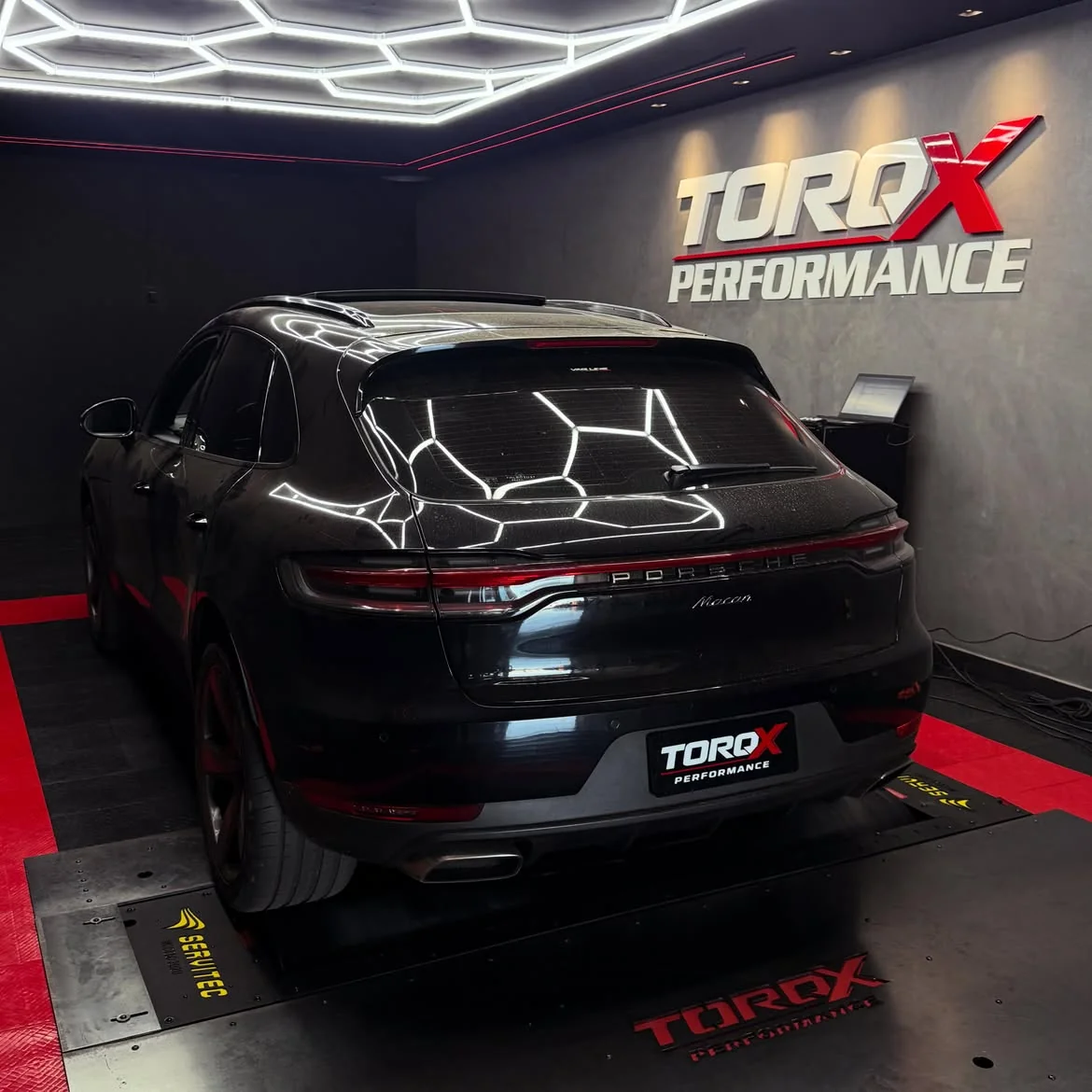 Porsche Macan preto de traseira na sala de dinamômetro, com a luminária hexagonal refletida na pintura