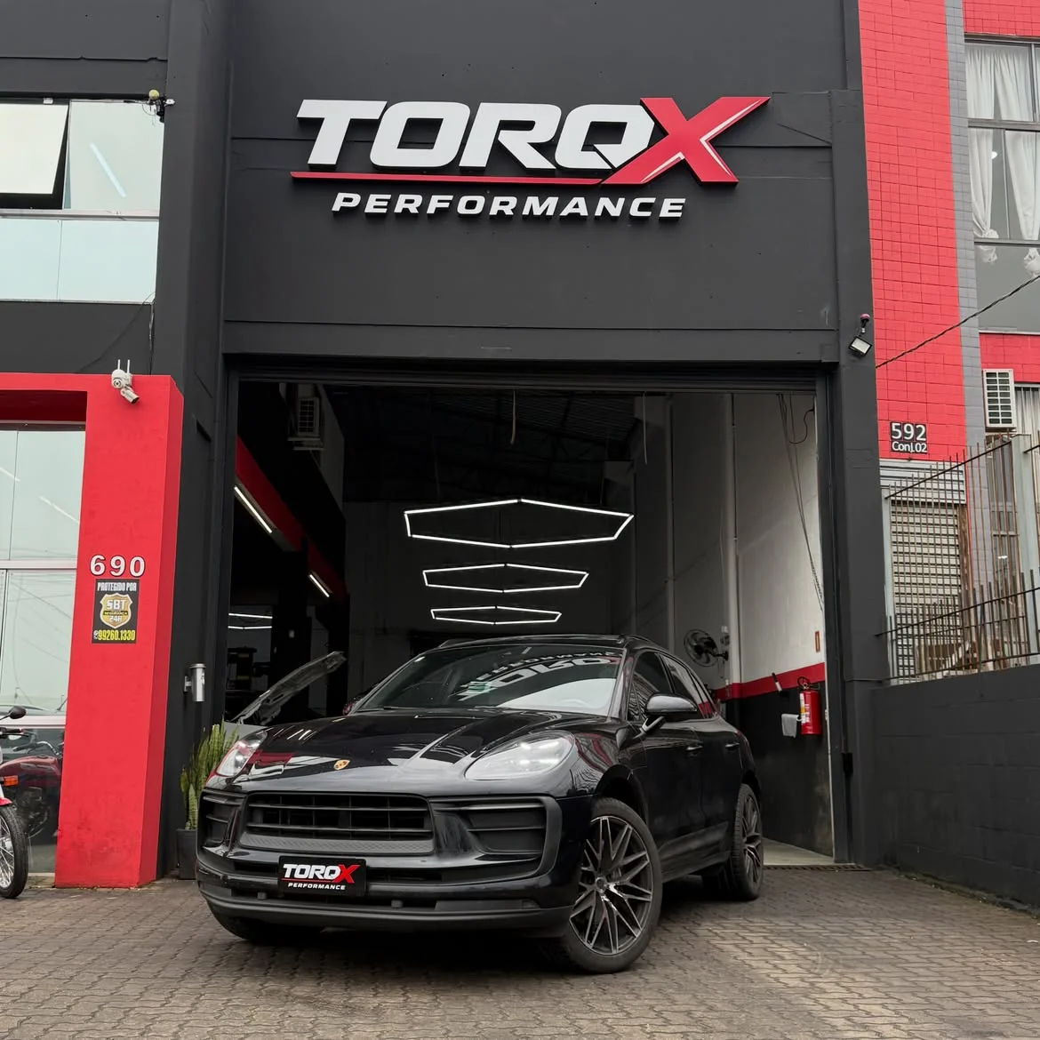 Porsche Macan preta parada sob o letreiro da fachada da TORQX, com o portão aberto e a oficina ao fundo