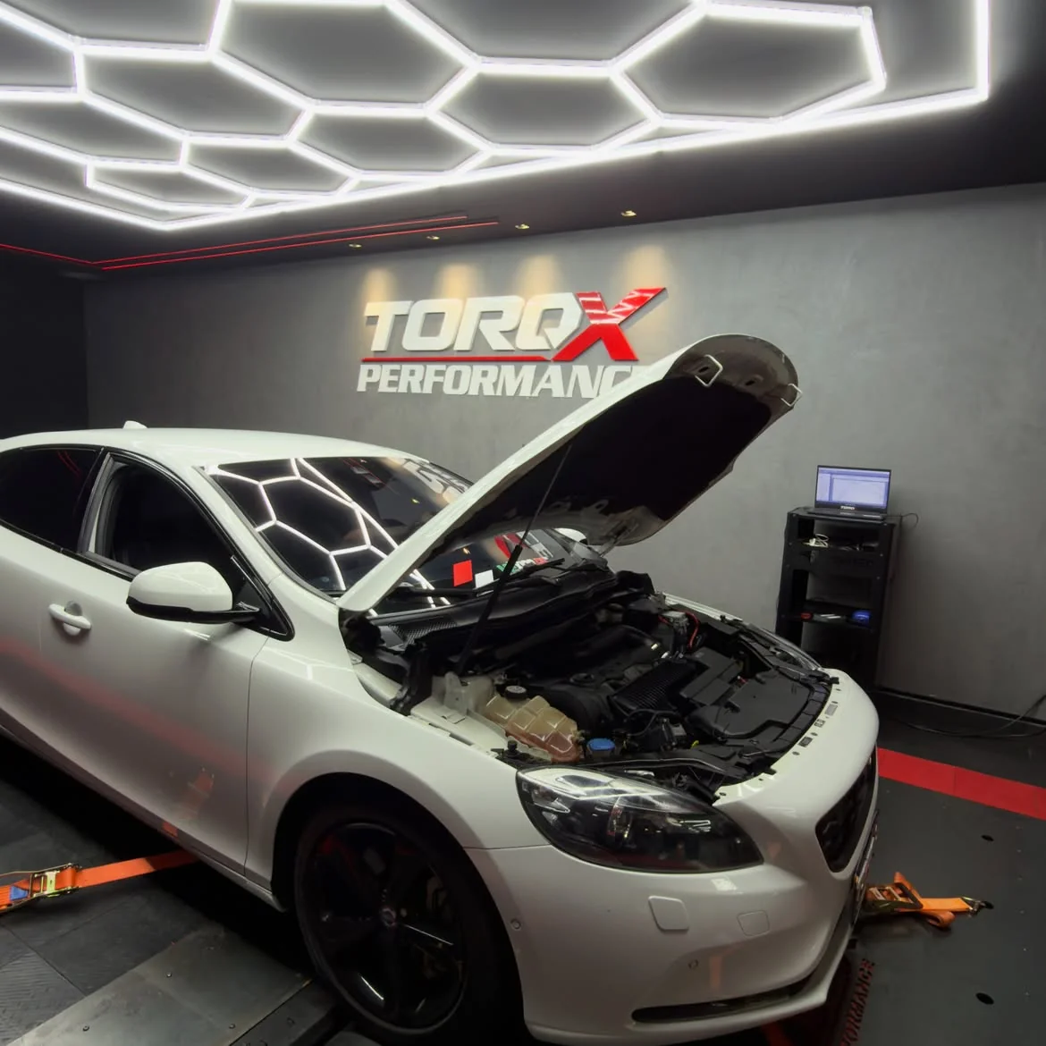 Volvo V40 branco com o capô levantado no dinamômetro, com o notebook de calibração no rack ao lado