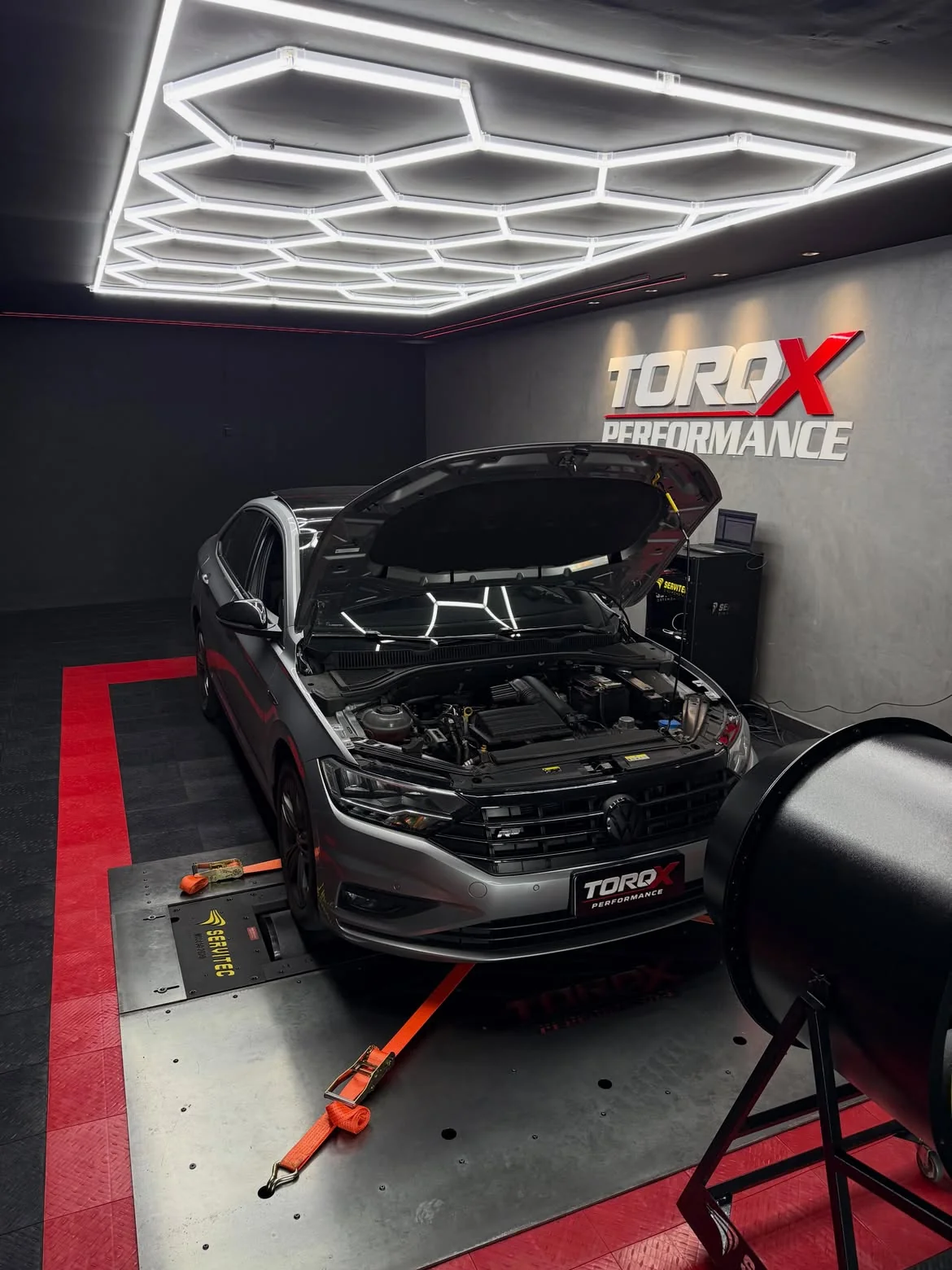 Volkswagen Jetta prata com o capô levantado no leito do dinamômetro, sob a luminária hexagonal da sala