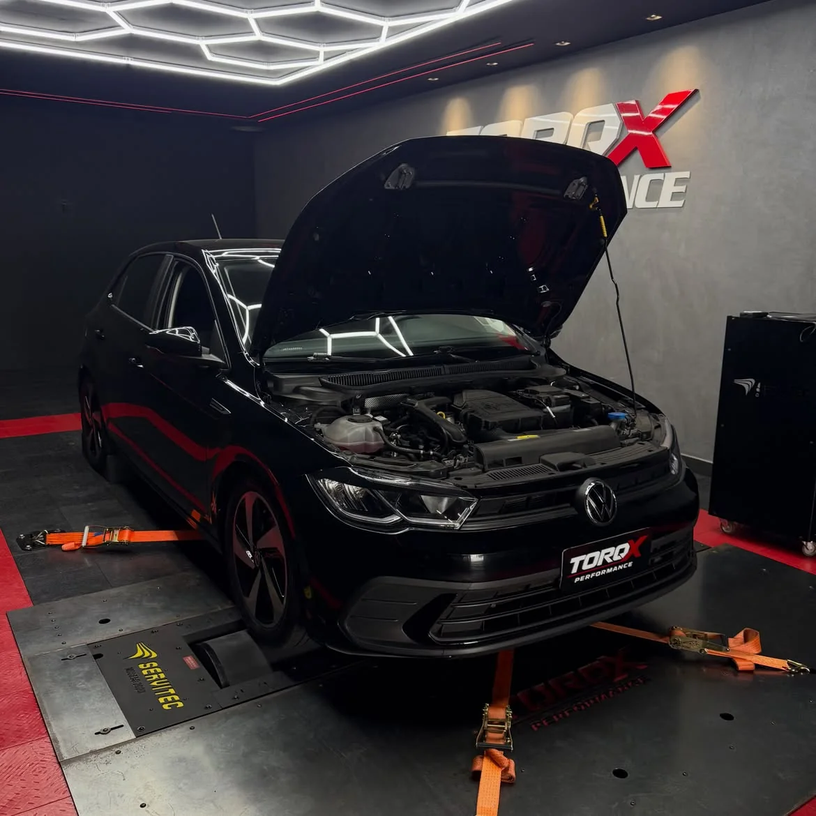 Volkswagen Polo preto de três quartos dianteiro com o capô levantado sobre o leito do dinamômetro