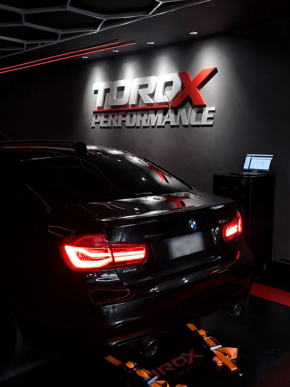 BMW ancorado no leito do dinamômetro sob o letreiro TORQX, com um notebook aberto em suporte atrás do veículo