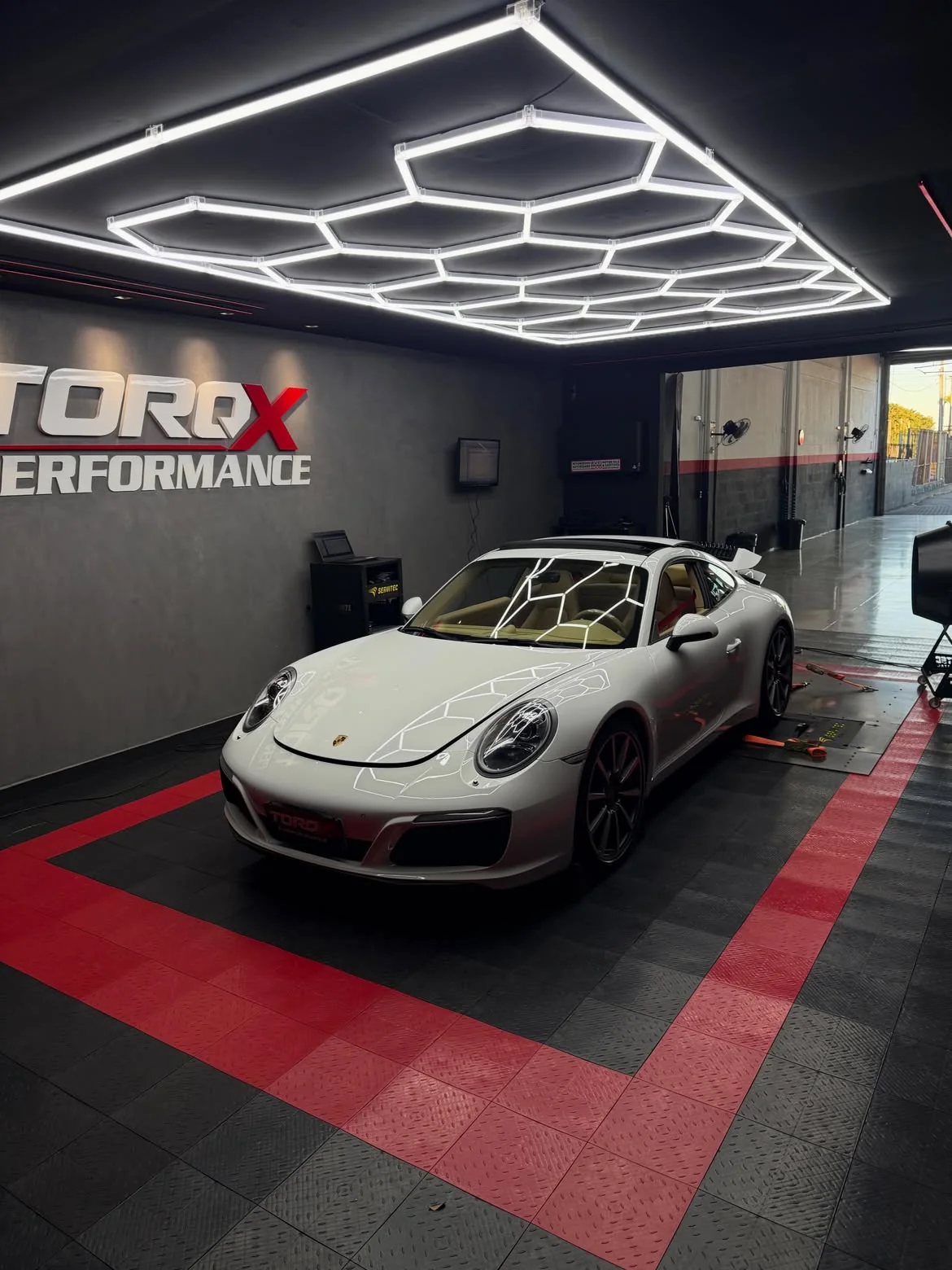 Porsche 911 branco sob a luminária hexagonal completa da sala de dinamômetro TORQX